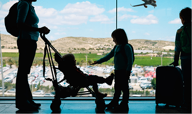 Silhouette of a woman with a stroller, a child beside her, and another person with a suitcase at an airport window. An airplane flies outside against a blue sky. Mortgage Broker Fremantle helps families prepare for big journeys.